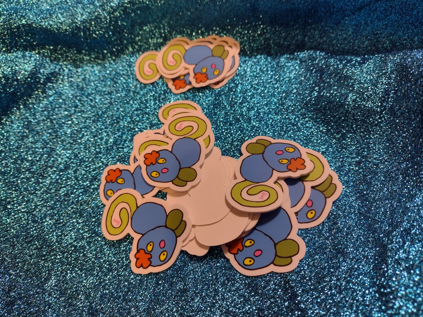 A bunch of blue Gralockamay stickers laid out on a blue sequence fabric.