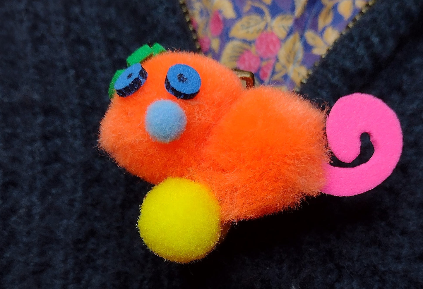 Orange Pom-Pom Gralockamay Pin with hot pink tail, yellow feet, a light blue nose dark blue eyes and a green flower looking crest.