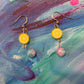Lemon Drop Earrings with a lemon slice made of Polymer clay and a multi colored glass bead. On a colorful canvases background.