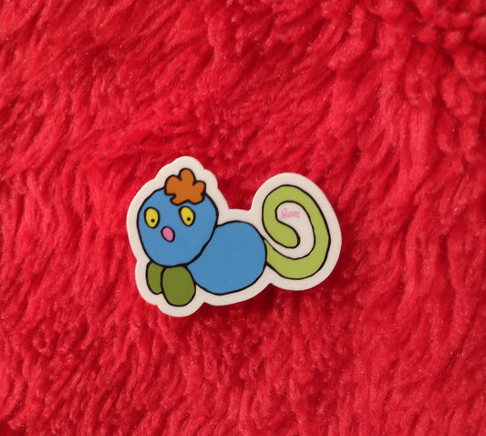 A blue Gralockamay sticker with a green curly tail an orange flower-tuft of hair. On a red fury background.
